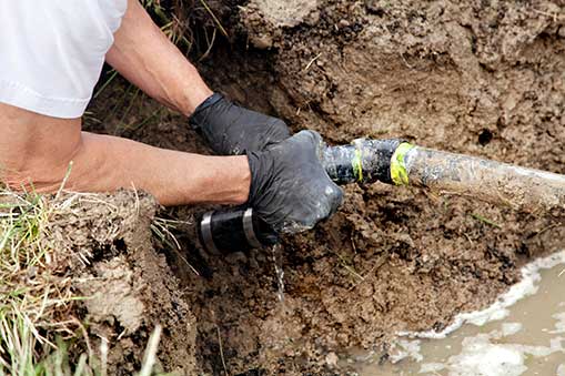 Plumber in gloves repairing a pipe during excavation, showcasing safe plumbing practices and precision in underground work.